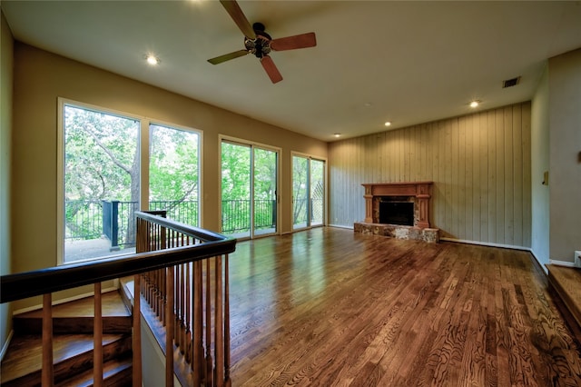 unfurnished living room featuring a stone fireplace, hardwood / wood-style flooring, ceiling fan, and wood walls