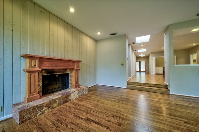 unfurnished living room with a stone fireplace, a skylight, wooden walls, and hardwood / wood-style flooring