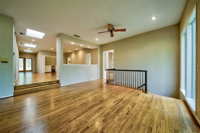 empty room featuring hardwood / wood-style flooring, ceiling fan, and a skylight