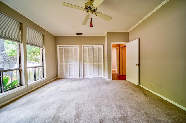 unfurnished bedroom featuring multiple closets, ceiling fan, crown molding, and light carpet