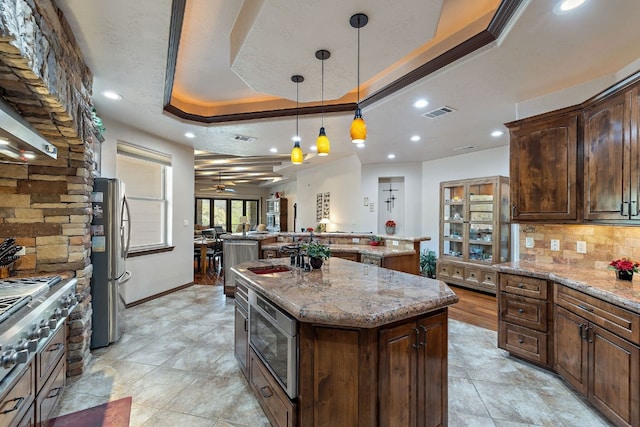 kitchen featuring appliances with stainless steel finishes, a kitchen island, backsplash, hanging light fixtures, and a tray ceiling