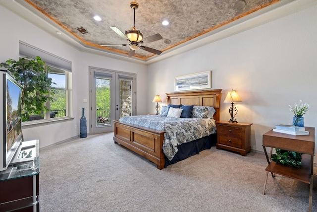 bedroom featuring french doors, access to exterior, ceiling fan, a tray ceiling, and light carpet