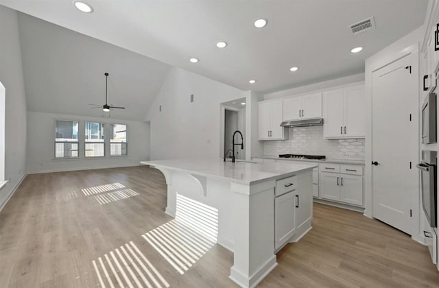 kitchen with vaulted ceiling, white cabinets, light hardwood / wood-style flooring, a kitchen island with sink, and sink