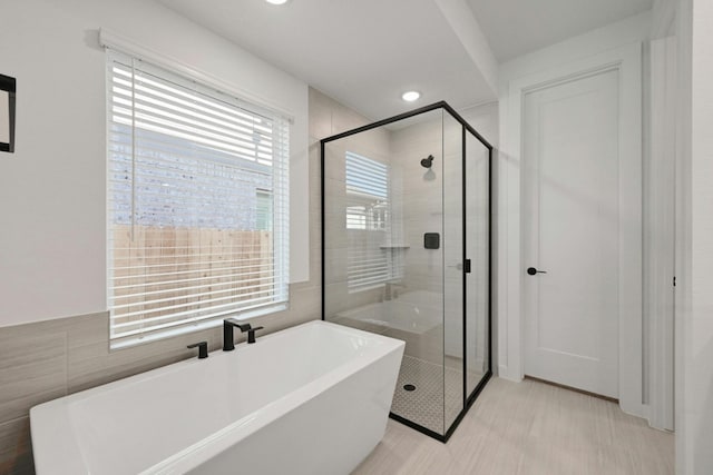 bathroom with independent shower and bath, tile walls, and a healthy amount of sunlight