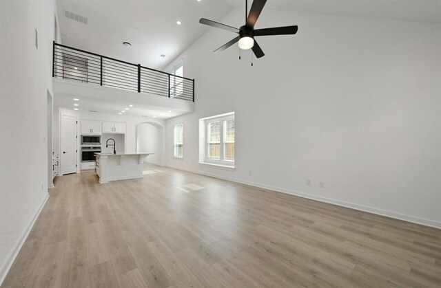 unfurnished living room featuring ceiling fan, sink, light hardwood / wood-style floors, and high vaulted ceiling