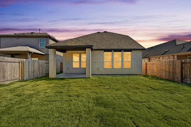 back house at dusk featuring a lawn and a patio area