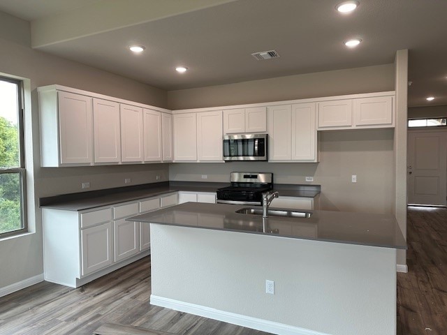 kitchen featuring a center island with sink, wood-type flooring, sink, stainless steel appliances, and white cabinets