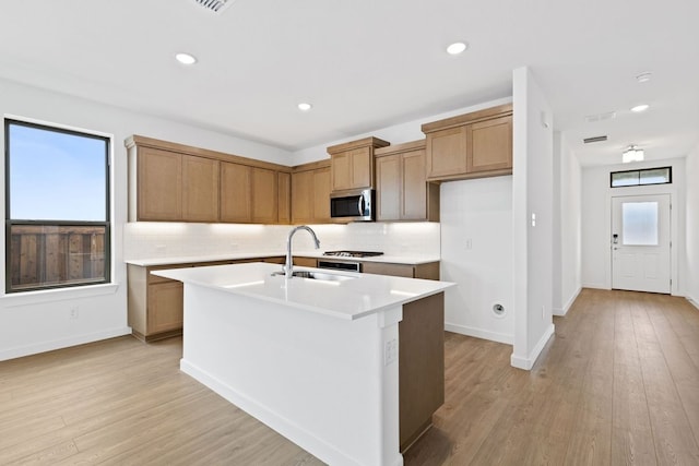 kitchen featuring sink, light hardwood / wood-style flooring, tasteful backsplash, and an island with sink