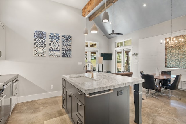 kitchen with ceiling fan with notable chandelier, an island with sink, decorative light fixtures, high vaulted ceiling, and sink