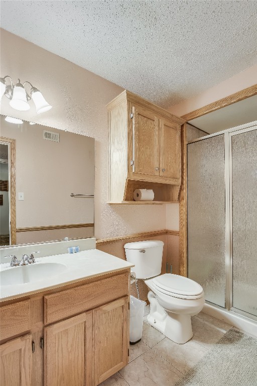 bathroom featuring tile patterned flooring, vanity, toilet, and a shower with shower door