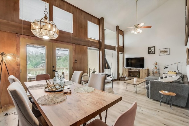 dining space with french doors, light hardwood / wood-style flooring, high vaulted ceiling, wooden walls, and ceiling fan with notable chandelier