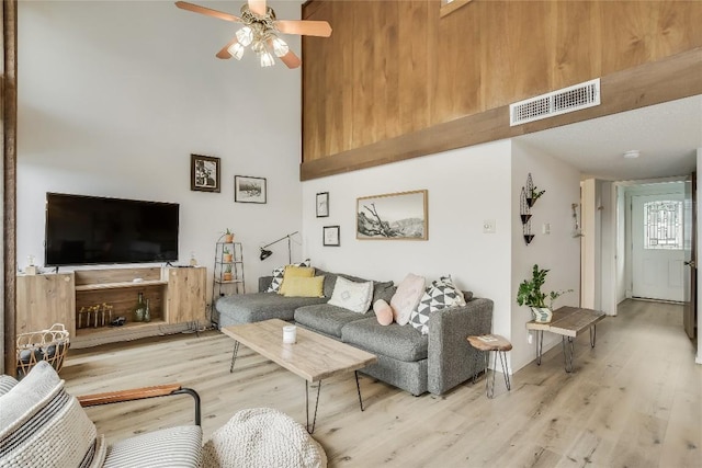 living room with ceiling fan, a towering ceiling, and light wood-type flooring