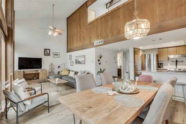 dining area with ceiling fan with notable chandelier, light wood-type flooring, and a high ceiling