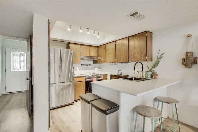 kitchen featuring a kitchen bar, appliances with stainless steel finishes, a textured ceiling, sink, and light hardwood / wood-style floors