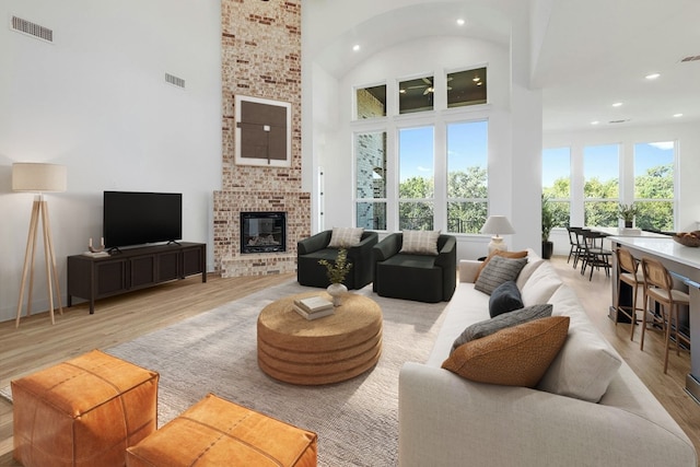 living room featuring a high ceiling, a fireplace, light hardwood / wood-style floors, and plenty of natural light