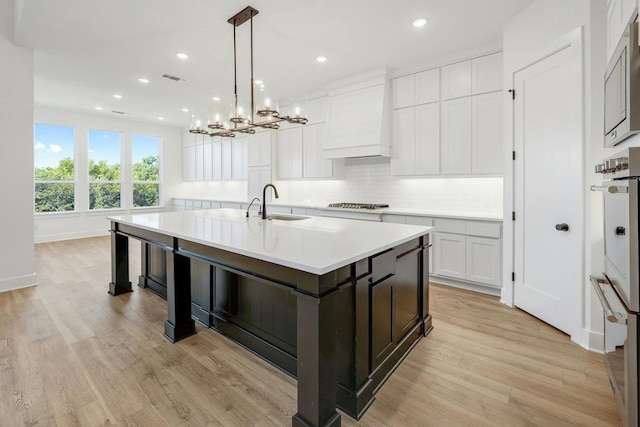 kitchen featuring light hardwood / wood-style floors, hanging light fixtures, an island with sink, and white cabinets