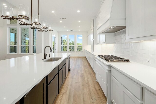 kitchen featuring custom exhaust hood, light wood-type flooring, sink, pendant lighting, and stainless steel appliances