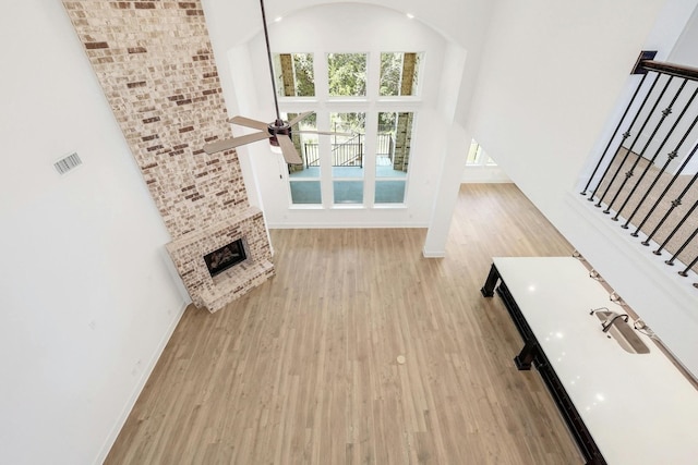 unfurnished living room with a high ceiling, a fireplace, light wood-type flooring, and ceiling fan