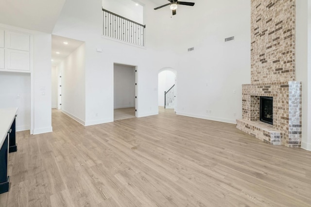 unfurnished living room with a high ceiling, a fireplace, light wood-type flooring, and ceiling fan