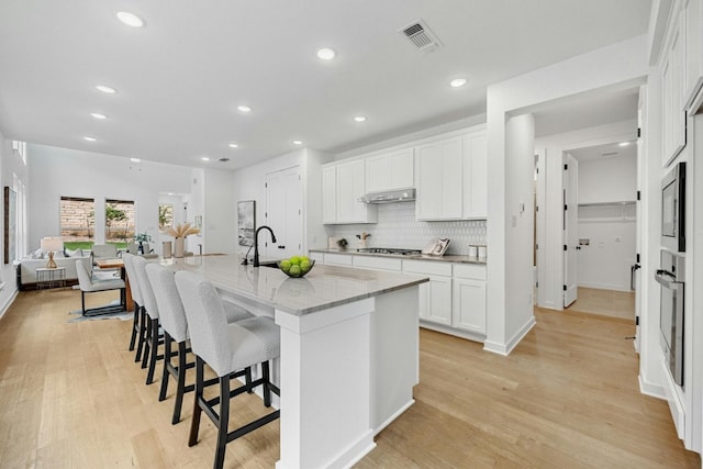 kitchen featuring white cabinets, light stone counters, a kitchen island with sink, and light hardwood / wood-style flooring