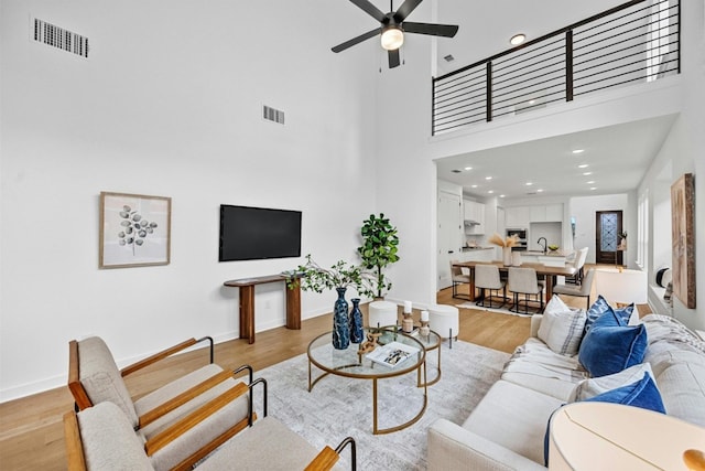 living room featuring a towering ceiling, ceiling fan, and light hardwood / wood-style floors