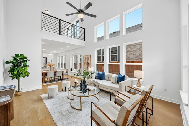 living room featuring light hardwood / wood-style flooring, ceiling fan, and a high ceiling