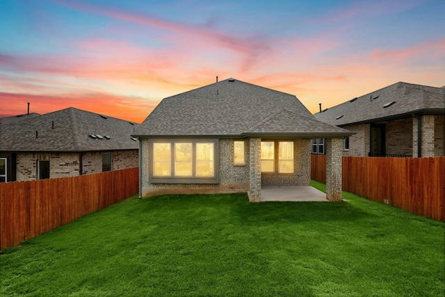 back house at dusk with a lawn and a patio