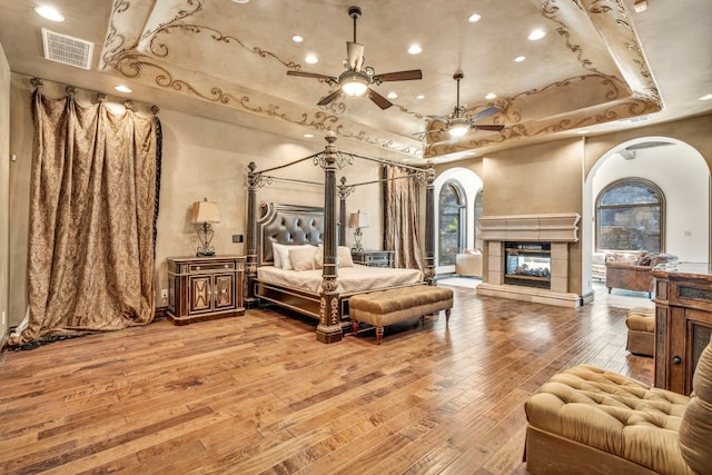 bedroom featuring wood-type flooring, a raised ceiling, and a tiled fireplace