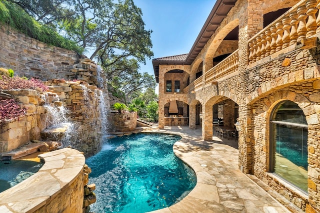 view of swimming pool featuring pool water feature, a patio, and an outdoor fireplace