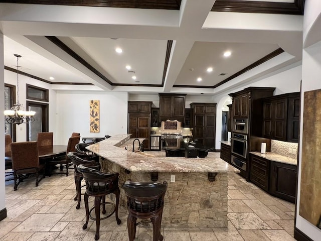 kitchen featuring an inviting chandelier, a kitchen breakfast bar, tasteful backsplash, light stone counters, and a large island with sink