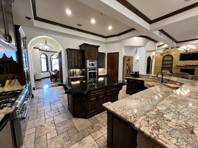 kitchen featuring dark brown cabinetry, high end stainless steel range, dark stone countertops, a stone fireplace, and a large island