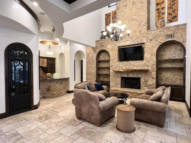 living room featuring a notable chandelier, a stone fireplace, and a towering ceiling