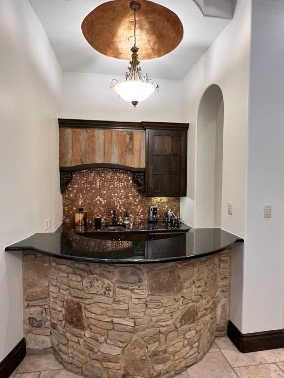 bar with decorative backsplash, dark stone counters, dark brown cabinetry, a tray ceiling, and decorative light fixtures