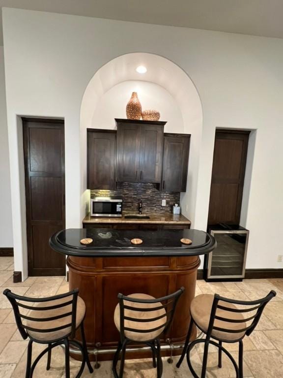 bar featuring backsplash and dark brown cabinets