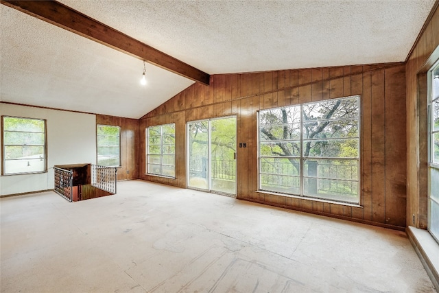 unfurnished living room with wood walls, lofted ceiling with beams, and a wealth of natural light