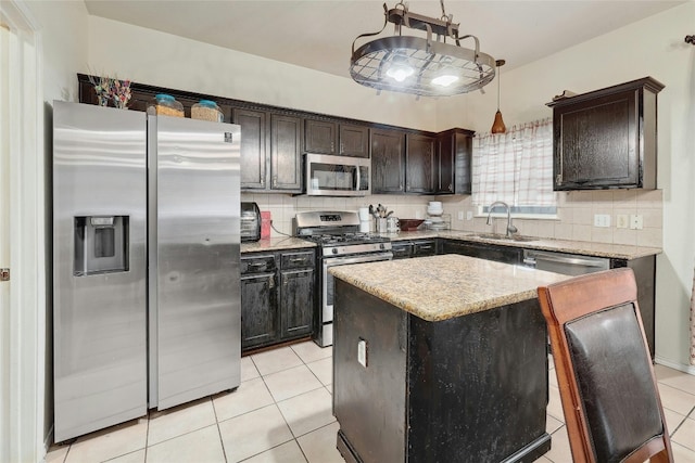 kitchen featuring sink, light stone counters, appliances with stainless steel finishes, backsplash, and a center island