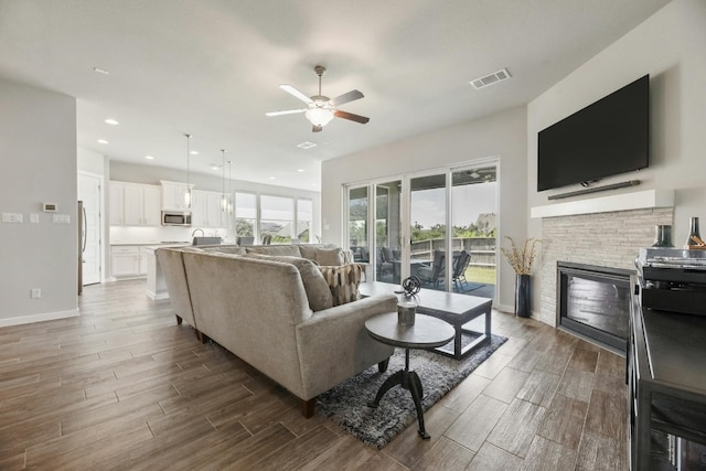 living room with a fireplace, ceiling fan, and wood-type flooring