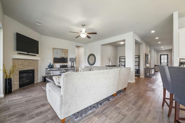 living room with light wood-type flooring, ceiling fan, and a fireplace