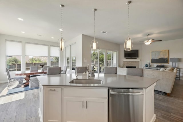 kitchen with hanging light fixtures, white cabinetry, light wood-type flooring, dishwasher, and a stone fireplace