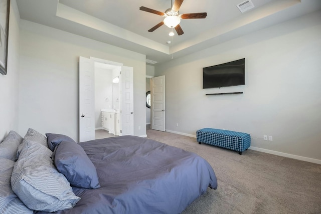 bedroom featuring a raised ceiling, ceiling fan, light colored carpet, and ensuite bathroom