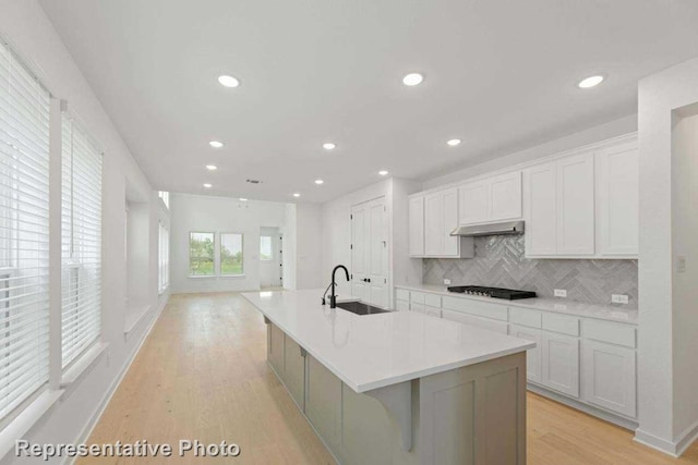 kitchen featuring a kitchen island with sink, white cabinets, sink, tasteful backsplash, and light hardwood / wood-style floors