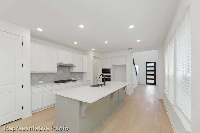 kitchen with white cabinets, stainless steel appliances, a center island with sink, and a healthy amount of sunlight