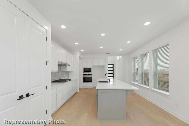 kitchen featuring a kitchen island with sink, white cabinets, appliances with stainless steel finishes, tasteful backsplash, and light hardwood / wood-style floors