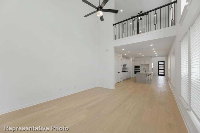 unfurnished living room featuring sink, ceiling fan, a high ceiling, and light wood-type flooring