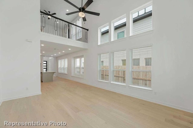 empty room with ceiling fan, light wood-type flooring, and a high ceiling