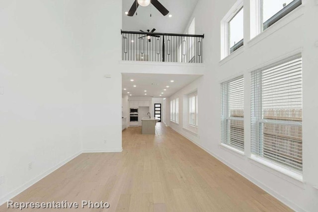 unfurnished living room with plenty of natural light, ceiling fan, a high ceiling, and light wood-type flooring