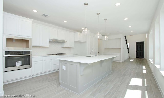 kitchen with white cabinets, sink, tasteful backsplash, stainless steel oven, and a center island with sink