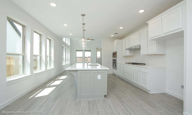 kitchen featuring a kitchen island with sink, a healthy amount of sunlight, stainless steel appliances, and white cabinetry