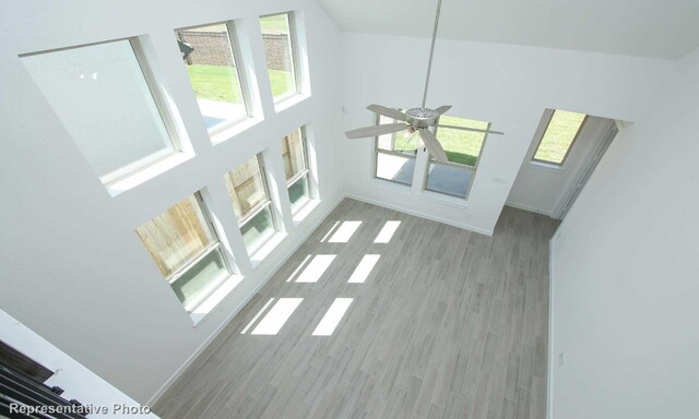 unfurnished living room featuring wood-type flooring, ceiling fan, and a high ceiling