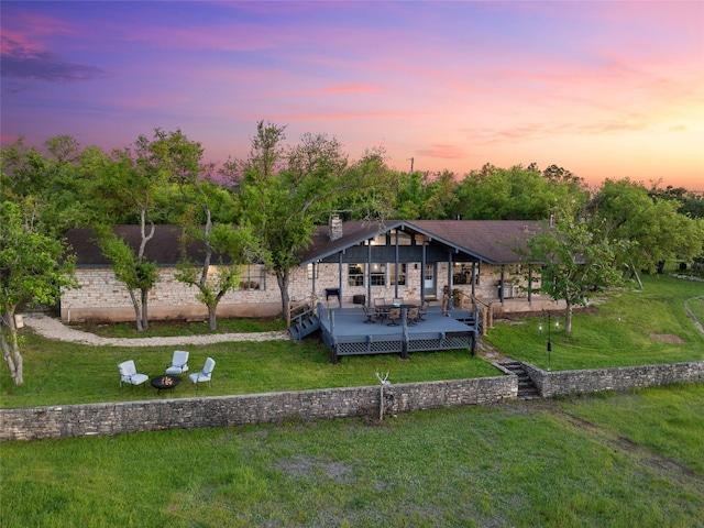 back house at dusk featuring a lawn and a deck